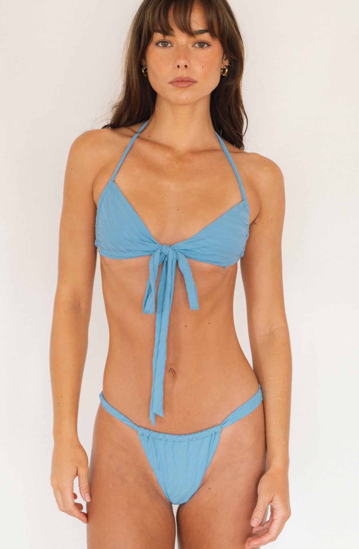 A woman modeling a light blue two-piece bikini with a halter top and matching side-tie bottoms against a plain white studio background.
