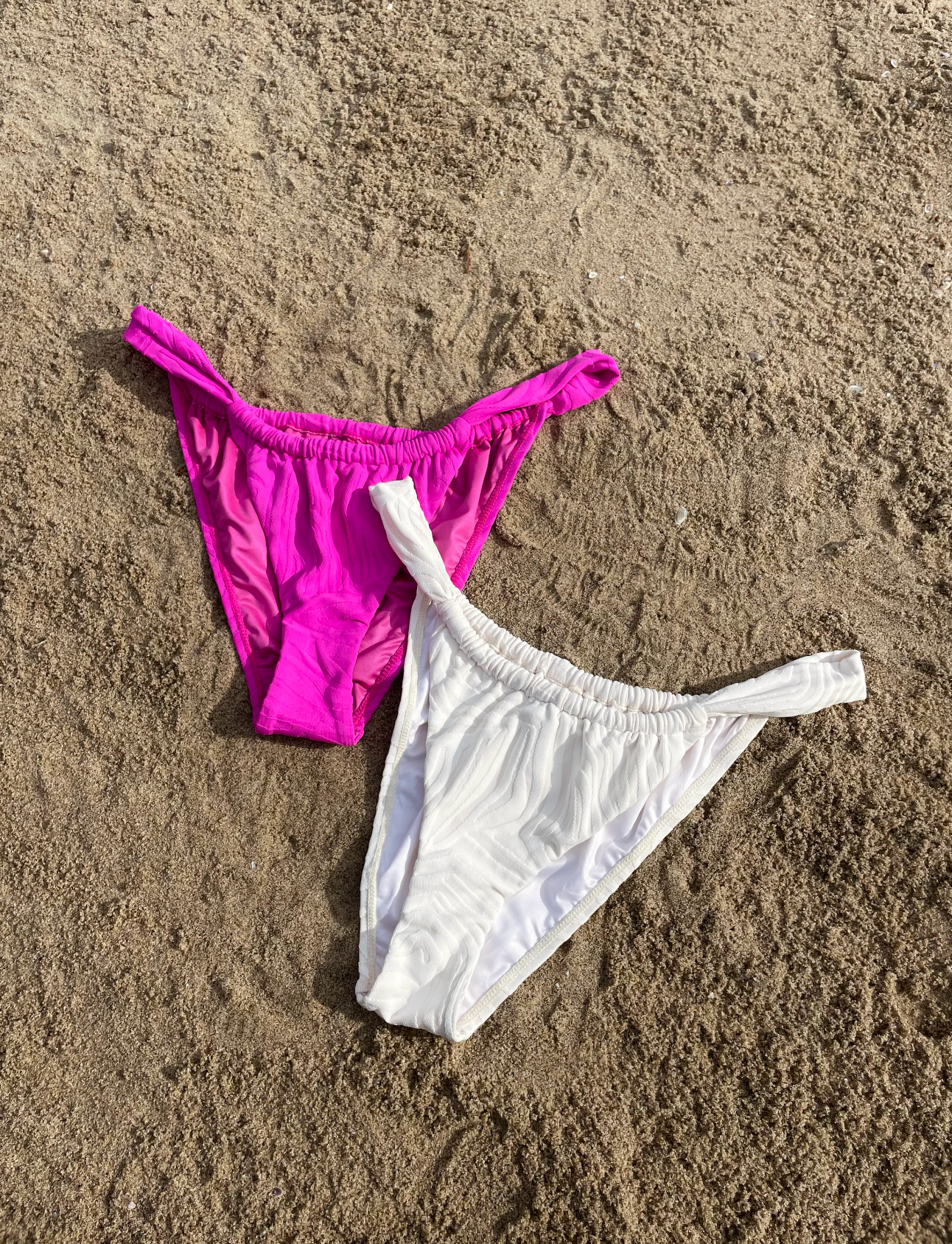 Two Bikini bottoms in white and pink lying on the sand
